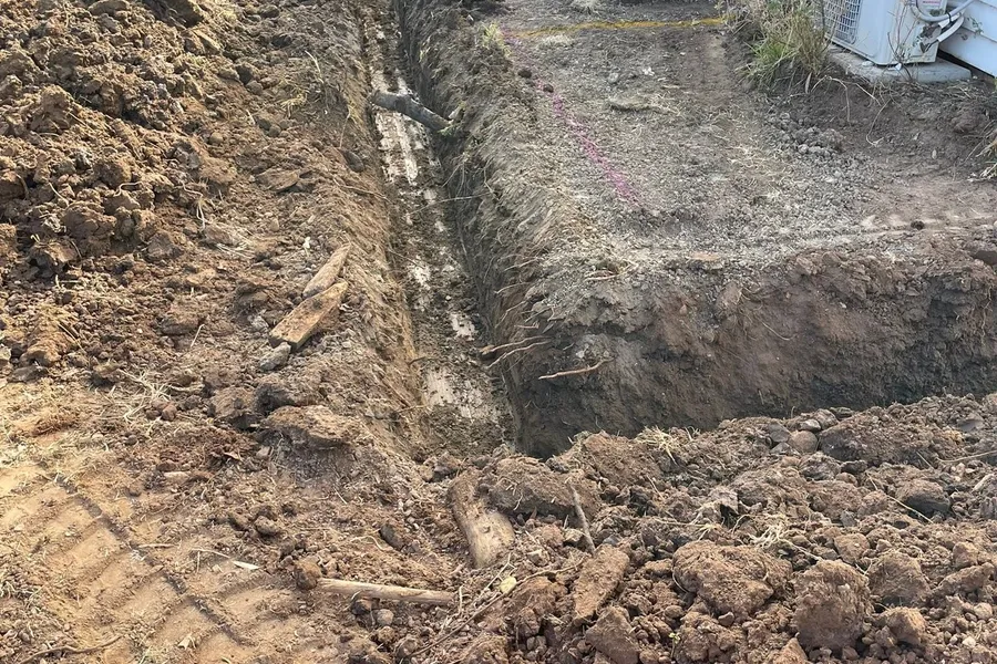 A narrow service trench dug across a residential yard ready for drainage pipe.
